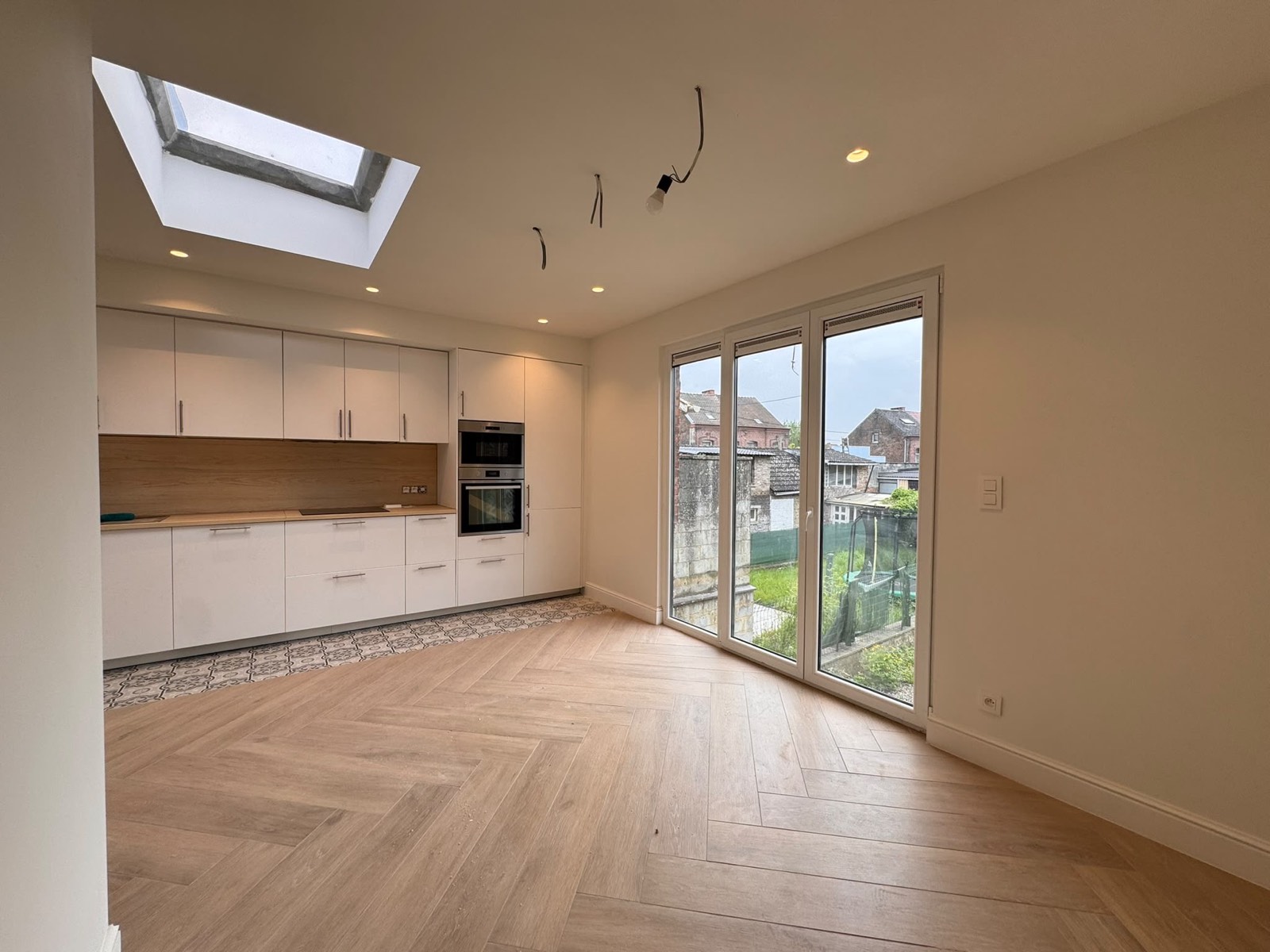 Cuisine blanche ouverte avec parquet posé en chevrons et grande baie vitrée